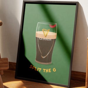 May include: Framed art print featuring a pint of Guinness with a red kiss mark on the glass. The artwork is set against a green background with the words "SPLIT THE G" in yellow. The print is displayed near a wooden chair.