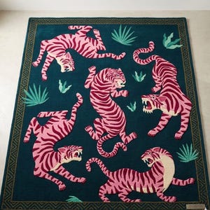 May include: A rectangular rug with a teal background featuring pink tigers with dark red stripes. The rug has a dark green border with a geometric pattern and green plant accents.