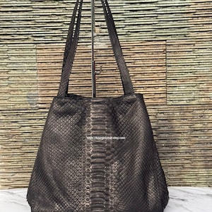 May include: A dark brown tote bag with a textured snakeskin pattern and a vertical central panel featuring larger, elongated scales. The bag has two long shoulder straps and displays the text https://luxegoodsid.etsy.com in the centre.