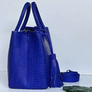 May include: A vibrant blue tote bag with matching handles and a detachable shoulder strap. The bag features a textured, snakeskin-like pattern and a decorative tassel. The bag is a stylish accessory.