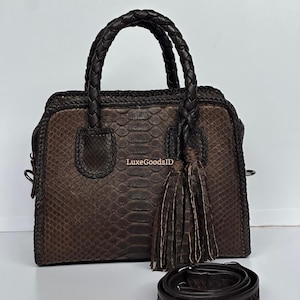 May include: Brown leather handbag with a braided handle and a detachable shoulder strap. The bag features a snakeskin pattern and a decorative tassel. The text "LuxeGoodsID" is visible on the bag.