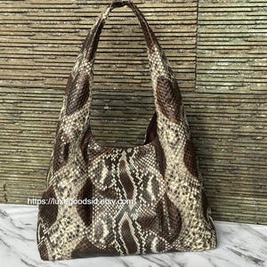 Puede incluir: Bolso de hombro marrón y beige con estampado de piel de serpiente y un asa. El bolso tiene forma redondeada y un interior espacioso. La URL de la tienda de Etsy es visible en la parte inferior izquierda de la imagen.