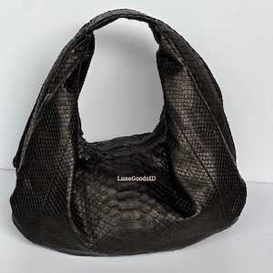 May include: A dark brown, large hobo bag with a textured, snakeskin-like pattern. The bag has a single shoulder strap and a slouchy design. The text "LuxeGoodsID" is visible on the bag.