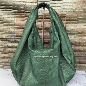 May include: A deep green hobo bag featuring a textured snakeskin pattern across the entire exterior. The bag has a slouchy, unstructured silhouette with a single integrated handle and the text https://luxegoodsid.etsy.com printed on it.