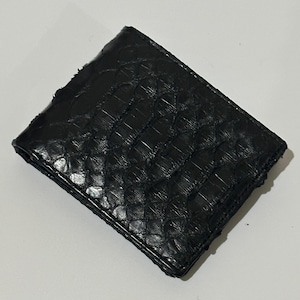 May include: A black leather wallet with a textured, scale-like pattern. The wallet is rectangular and appears to be folded, with visible stitching along the edges. The overall design is simple and classic.