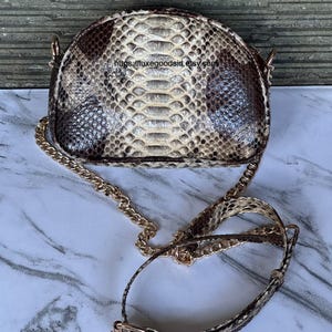 Peut inclure: Petit sac &agrave; main en forme de demi-lune avec un motif peau de serpent dans les tons marron, beige et cr&egrave;me. Le sac est dot&eacute; d'une bandouli&egrave;re cha&icirc;ne dor&eacute;e et d'une bandouli&egrave;re assortie en peau de serpent. Fermoir et accessoires dor&eacute;s.