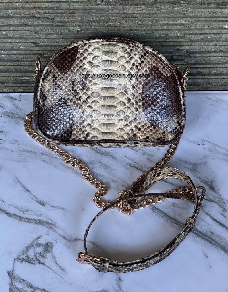 Peut inclure: Petit sac &agrave; main en forme de demi-lune avec un motif peau de serpent dans les tons marron, beige et cr&egrave;me. Le sac est dot&eacute; d'une bandouli&egrave;re cha&icirc;ne dor&eacute;e et d'une bandouli&egrave;re assortie en peau de serpent. Fermoir et accessoires dor&eacute;s.