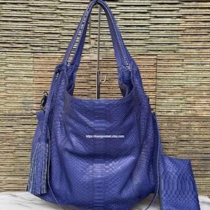 May include: A deep blue hobo bag with a textured snakeskin pattern, featuring two top handles, a side tassel, and a matching rectangular pouch. The text https://luxegoodsid.etsy.com is printed on the front of the bag. The bag has a slouchy shape.