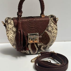 May include: A brown and beige snakeskin handbag with a rounded shape and a top handle. The bag features a flap closure, a tassel, and a detachable shoulder strap. The hardware is gold-toned.
