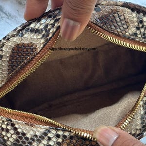Peut inclure: Sac &agrave; main rond avec un motif peau de serpent marron, beige et noir. Il est dot&eacute; d'une fermeture &eacute;clair dor&eacute;e et d'une bandouli&egrave;re cha&icirc;ne dor&eacute;e. L'int&eacute;rieur est de couleur marron clair. Le sac est ouvert.