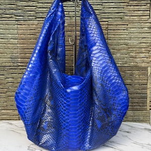 May include: A hobo-style handbag crafted from vibrant blue snakeskin leather. The bag features a distinct, repeating scale pattern with deep black accents between the scales, creating a textured, glossy appearance throughout the entire surface.
