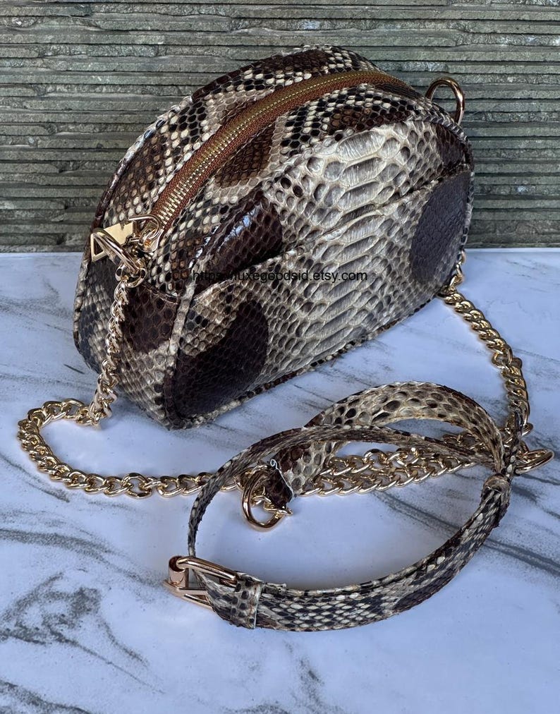 Peut inclure: Sac bandouli&egrave;re &agrave; motif peau de serpent avec une cha&icirc;ne dor&eacute;e et une fermeture &eacute;clair. Le sac pr&eacute;sente un motif marron, beige et noir. La bandouli&egrave;re comprend une section &agrave; motif peau de serpent avec une boucle dor&eacute;e.
