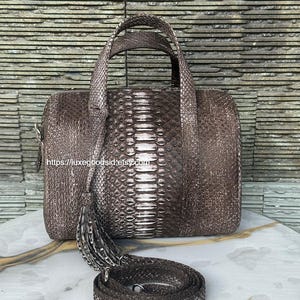 Może przedstawiać: Brązowa torebka o fakturze skóry węża z pasującym paskiem na ramię i ozdobnym chwostem. Torba ma prostokątny kształt z górnym uchwytem. Powierzchnia torby ma wzór łusek. Widoczny jest adres URL sklepu Etsy.