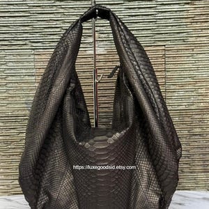 May include: A dark brown hobo bag with a textured snakeskin pattern and a single integrated shoulder strap. The bag features a slouchy, unstructured silhouette and includes the text https://luxegoodsid.etsy.com printed on the front surface.