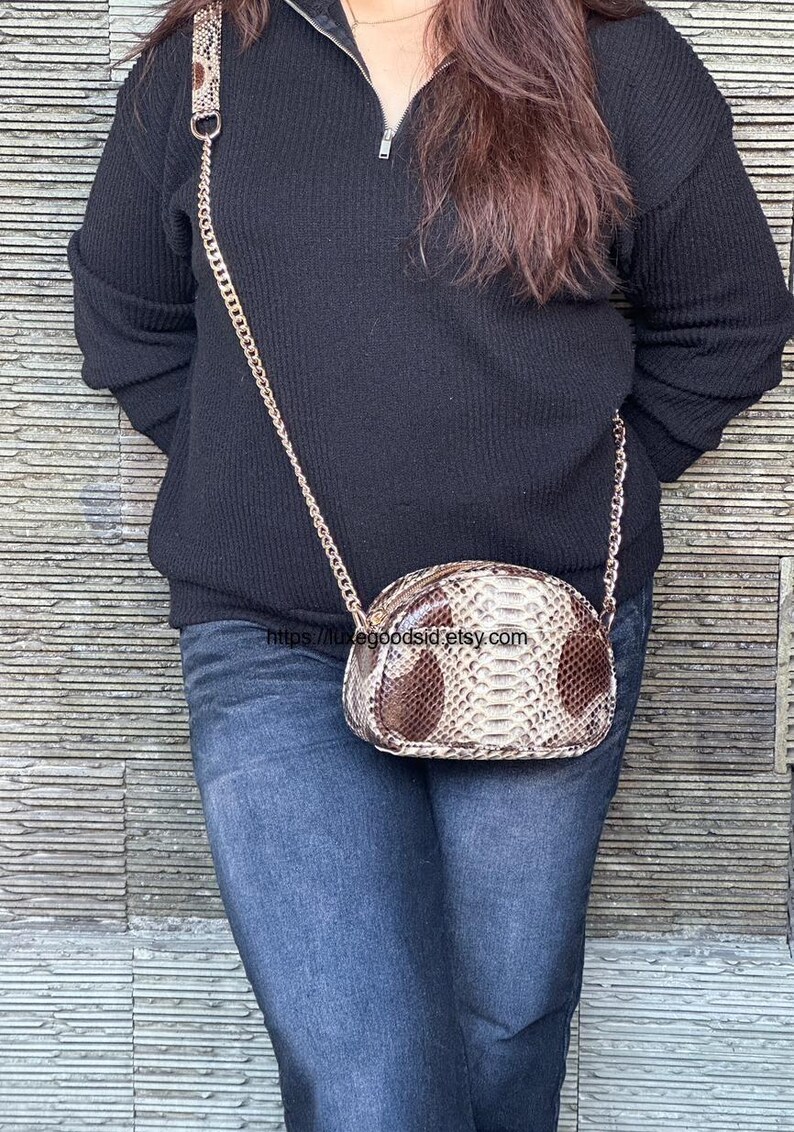 Peut inclure: Petit sac &agrave; main ovale avec un motif peau de serpent marron et cr&egrave;me. Il est dot&eacute; d'une bandouli&egrave;re dor&eacute;e et d'une fermeture &eacute;clair. Le sac est port&eacute; &agrave; l'&eacute;paule. Dimensions: environ 20 cm de long.