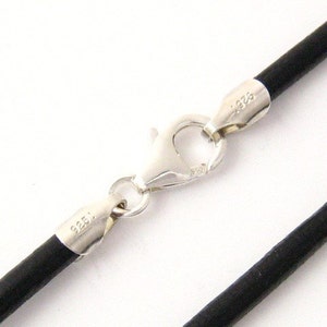 Puede incluir: Primer plano de un collar de cordón de cuero negro con un cierre plateado. El cierre es de tipo mosquetón y el cordón tiene aproximadamente 2 mm de diámetro. El cierre plateado está estampado con "925".