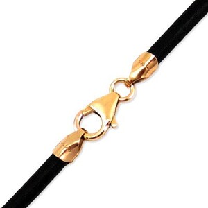 May include: A close-up shot of a black cord necklace with a gold-coloured clasp. The clasp is a lobster claw style, and the cord appears to be made of a soft, flexible material. The necklace is shown against a white background.