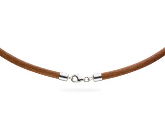 Puede incluir: Un collar de ante marrón con un cierre plateado. El collar tiene un diseño simple y minimalista, con un cordón redondo y un cierre seguro. El cierre plateado está conectado al cordón de ante con extremos plateados.