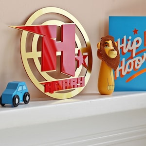 May include: Gold circle with a red letter H and the name Harry in red letters. A lion figurine and a blue card with the text "Hip Hoo" are in the background.