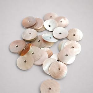 Peut inclure: Un ensemble de boutons circulaires en nacre, chacun doté d'un trou central unique. Ces disques en coquillage irisé présentent des variations naturelles de couleur, allant du crème et beige doux aux tons rose et brun clair subtils.