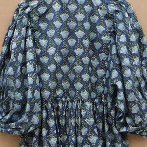 May include: A blue floral print dress with long, puffed sleeves. The dress features a repeating pattern of light blue flowers and green leaves on a dark blue background. It has a gathered waist and a round neckline.