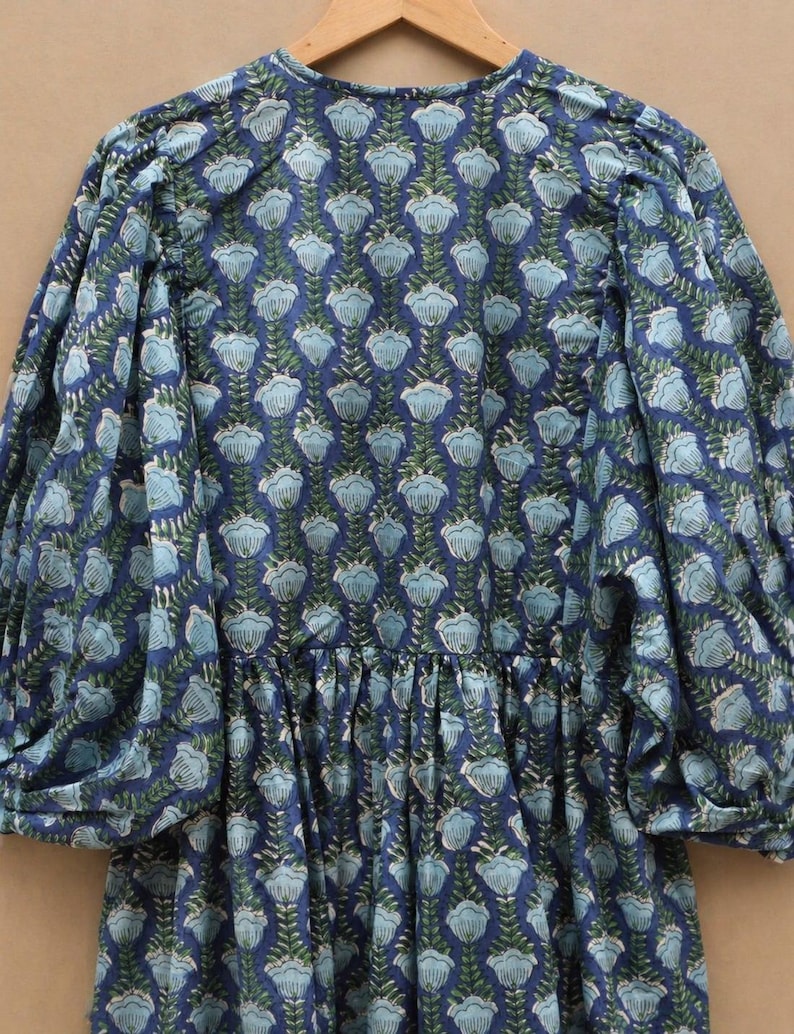May include: A blue floral print dress with long, puffed sleeves. The dress features a repeating pattern of light blue flowers and green leaves on a dark blue background. It has a gathered waist and a round neckline.