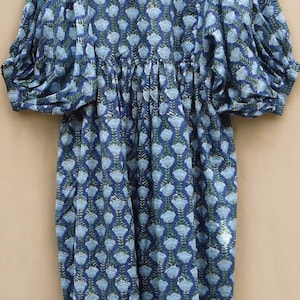 May include: A blue floral print dress with long, puffed sleeves. The dress has a repeating pattern of light blue flowers and green leaves on a darker blue background. It features a gathered waist and a loose, flowing skirt.
