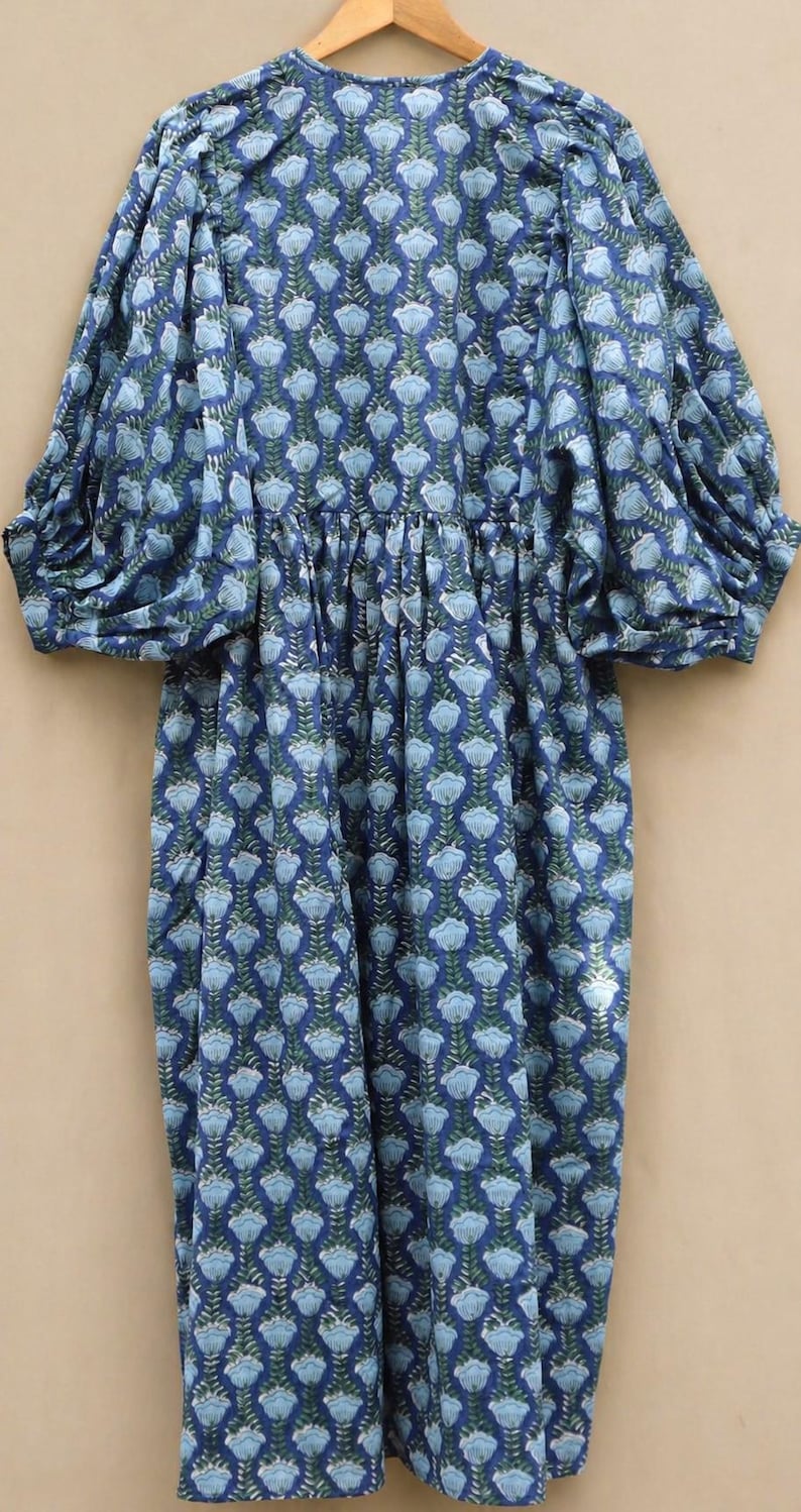 May include: A blue floral print dress with long, puffed sleeves. The dress has a repeating pattern of light blue flowers and green leaves on a darker blue background. It features a gathered waist and a loose, flowing skirt.