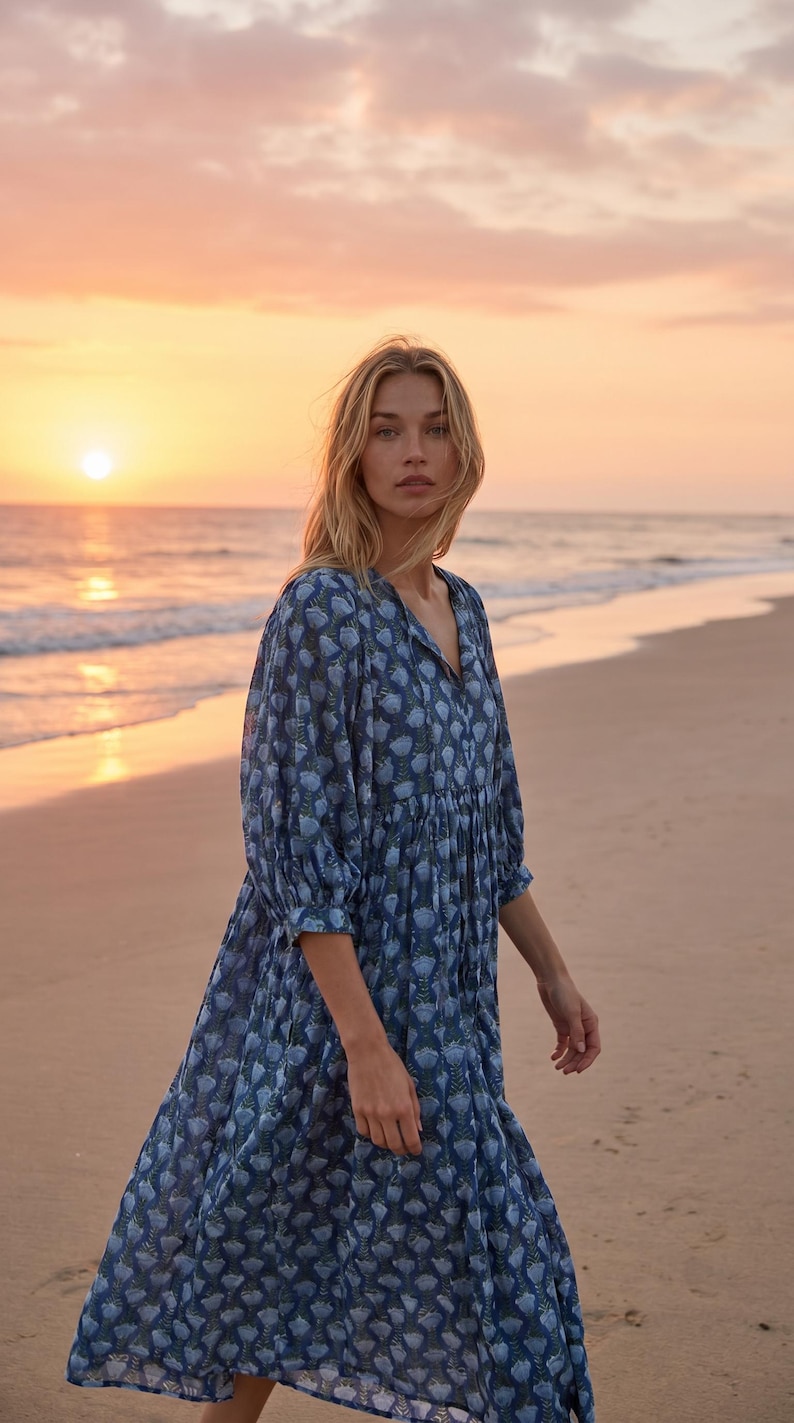 May include: A blue floral print dress with a V-neck and three-quarter sleeves. The dress is knee-length and has a tiered skirt. The background shows a beach scene with a sunset.