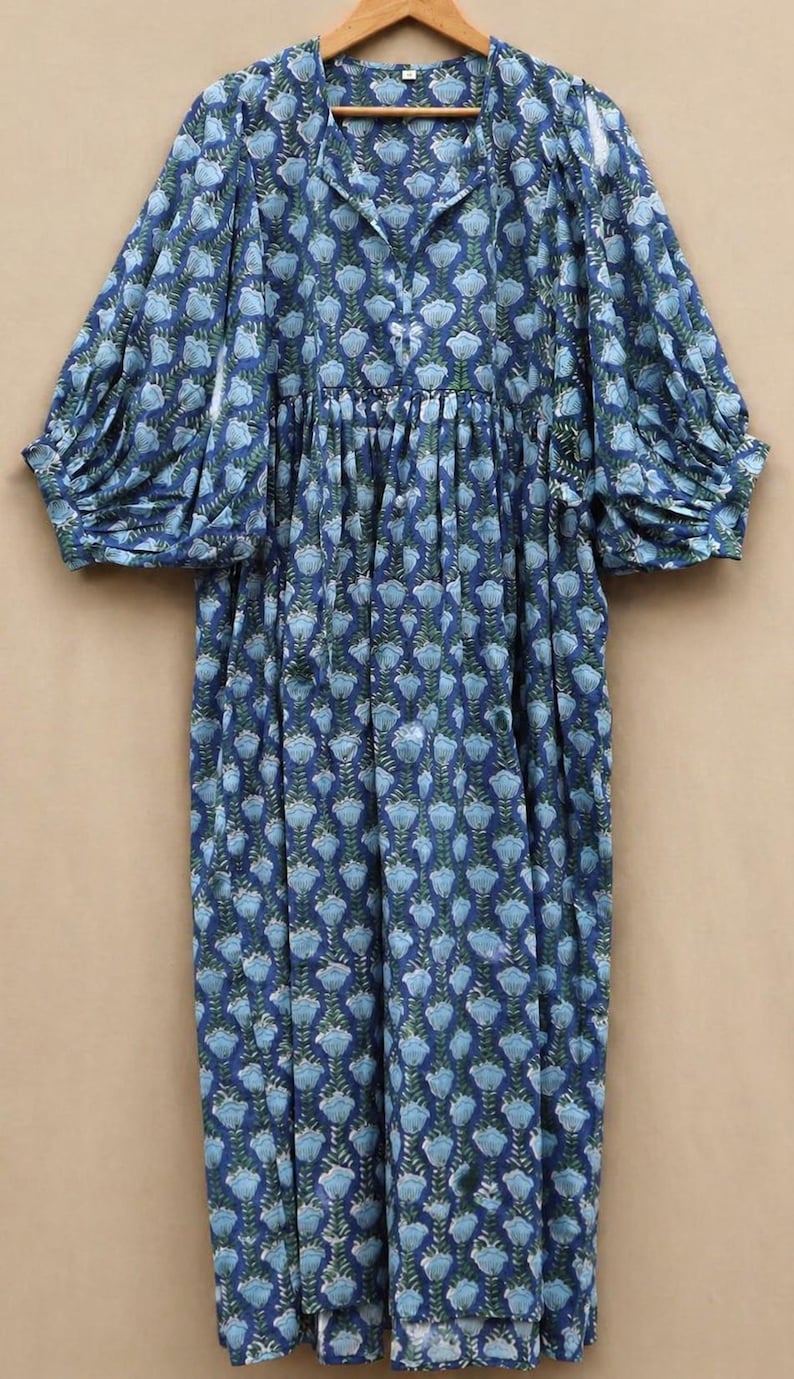 May include: A blue floral print dress with long, gathered sleeves. The dress has a V-neck and a full, flowing skirt. The fabric is patterned with light blue flowers and green leaves on a dark blue background.