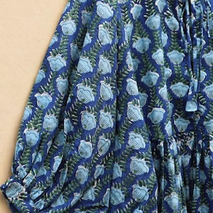 May include: A blue floral print dress with long sleeves. The dress features a repeating pattern of light blue flowers and green leaves on a dark blue background. The sleeves are gathered at the cuffs.