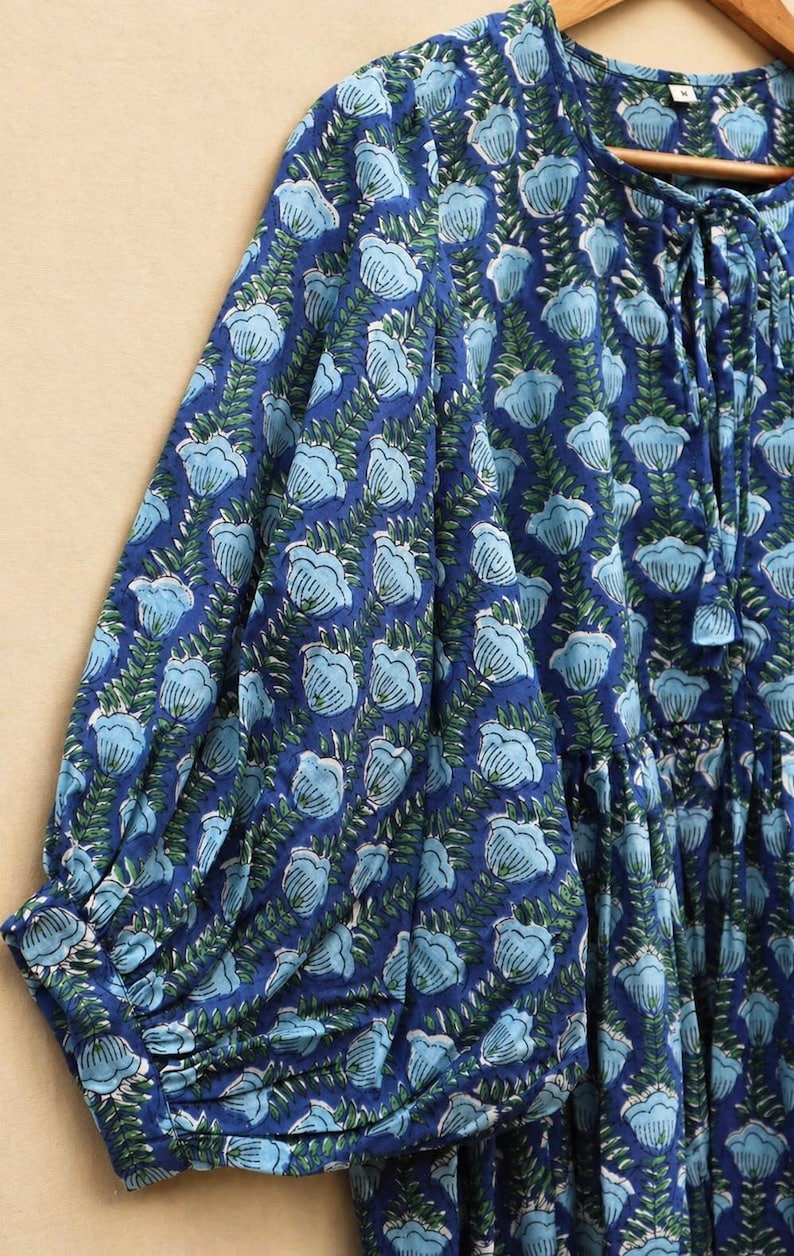 May include: A blue floral print dress with long sleeves. The dress features a repeating pattern of light blue flowers and green leaves on a dark blue background. The sleeves are gathered at the cuffs.