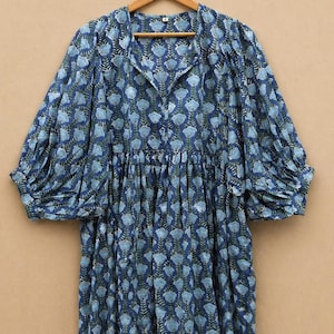 May include: A blue floral print dress with long, voluminous sleeves. The dress has a collared neckline and a gathered waist. The fabric features a pattern of light blue flowers and green leaves on a dark blue background. The dress is hanging on a wooden hanger.