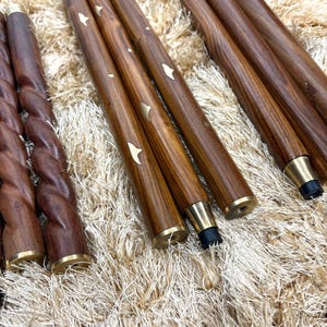 May include: A collection of wooden furniture legs with brass accents. Some legs are smooth, while others have a twisted design. Several legs have a star-shaped inlay. The legs are a rich brown color.