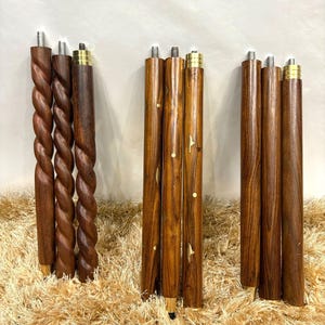 May include: A collection of wooden furniture legs in various designs. Some legs have a twisted rope design, while others are straight with decorative inlays. All legs have metal threaded tops and brass-colored accents.