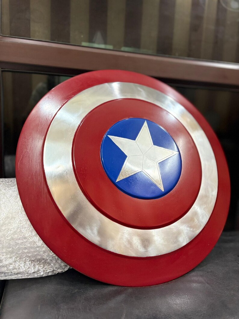 K&ouml;nnte beinhalten: Ein runder Schild mit einem roten Au&szlig;enring, einem silbernen Mittelring und einer blauen Mitte. Ein wei&szlig;er Stern befindet sich in der Mitte des blauen Kreises. Der Schild ist eine Nachbildung von Captain Americas Schild.