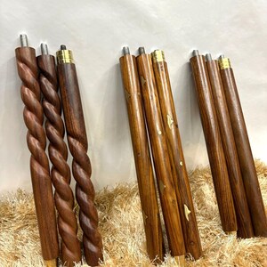 May include: A collection of wooden furniture legs in various designs. Some legs feature a twisted rope design, while others are straight with brass accents and decorative inlays. The legs are a rich brown color, suggesting a natural wood finish.