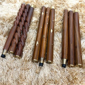 May include: A collection of wooden furniture legs in various designs. Some legs have a twisted rope design, while others are straight with brass accents and star-shaped inlays. The legs are a rich brown color and have black rubber feet.