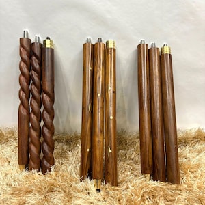 May include: A collection of wooden furniture legs in various designs. Some legs have a twisted rope design, while others are smooth with inlaid accents. All legs have brass-colored metal accents at the top and bottom. The legs are a rich brown color.