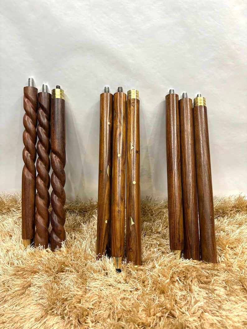 May include: A collection of wooden furniture legs in various designs. Some legs have a twisted rope design, while others are smooth with inlaid accents. All legs have brass-colored metal accents at the top and bottom. The legs are a rich brown color.
