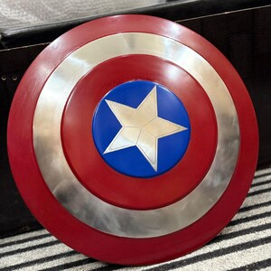 K&ouml;nnte beinhalten: Ein runder Schild mit einem roten Au&szlig;enring, einem silbernen Mittelring und einer blauen Mitte. Ein wei&szlig;er Stern befindet sich in der Mitte des blauen Kreises. Der Schild ist eine Nachbildung von Captain Americas Schild.