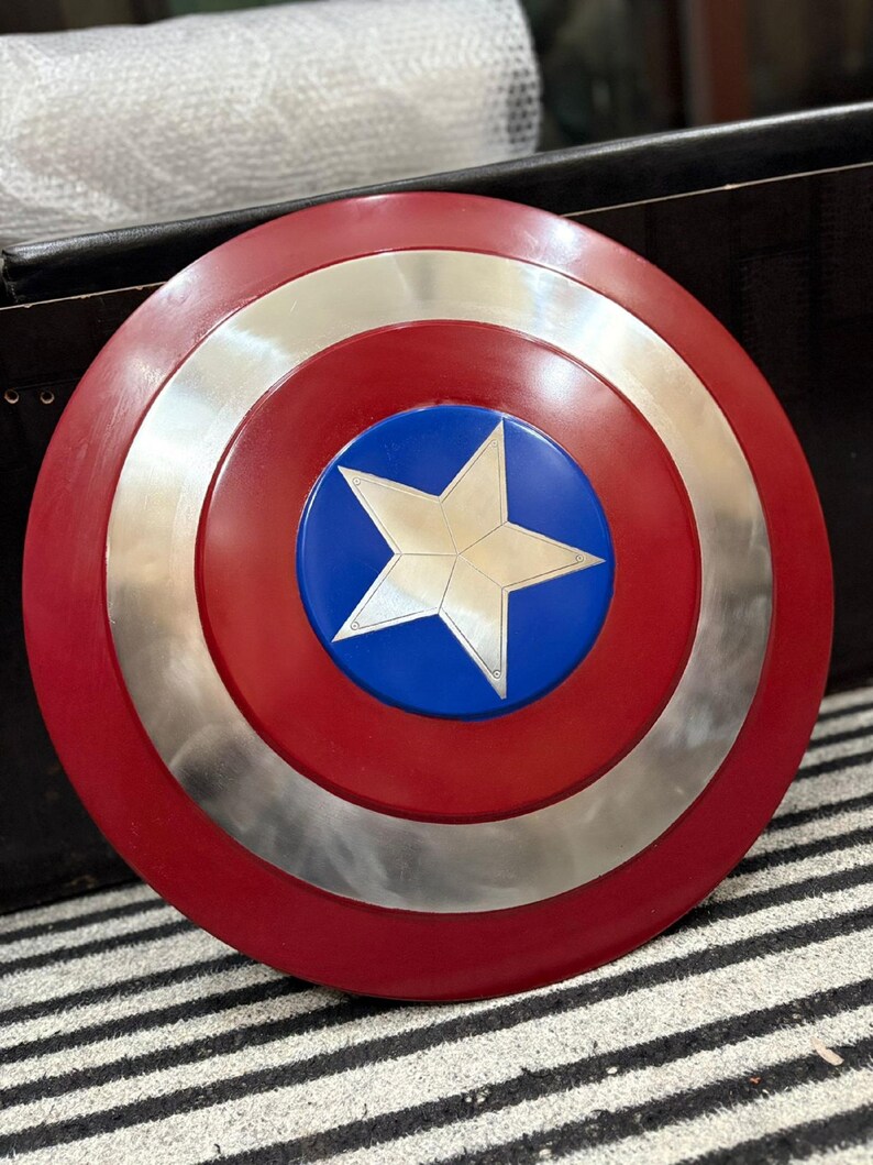 K&ouml;nnte beinhalten: Ein runder Schild mit einem roten Au&szlig;enring, einem silbernen Mittelring und einer blauen Mitte. Ein wei&szlig;er Stern befindet sich in der Mitte des blauen Kreises. Der Schild ist eine Nachbildung von Captain Americas Schild.