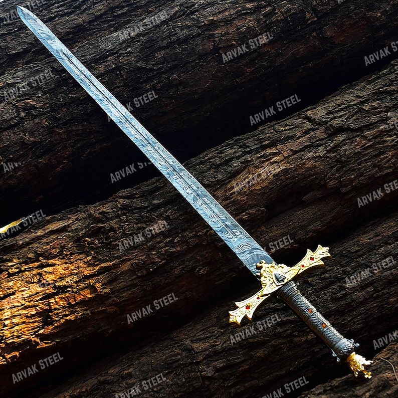 May include: A long, ornate sword with a patterned blade and gold-colored hilt. The hilt features red accents and a detailed design. The sword is displayed against a dark, textured wooden background.
