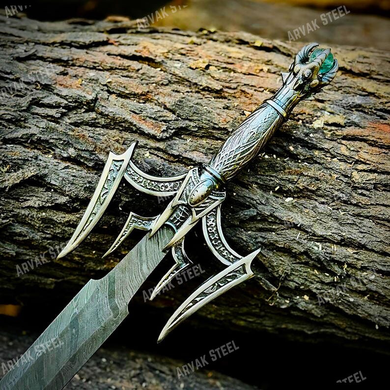 May include: A detailed, ornate sword with a silver-colored handle and blade. The handle features intricate carvings and a green gem at the pommel. The blade has a textured pattern. The sword is displayed on a weathered wooden surface.