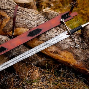 May include: A detailed image of a sword with a patterned blade and a black handle. The sword rests on a wooden log alongside a brown leather sheath with black accents. The sword's hilt has a silver finish with gold details.