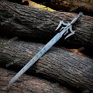 May include: A decorative sword with a patterned blade and ornate hilt. The hilt features a detailed design with a green accent. The blade has a unique, textured pattern. The sword is displayed on a bed of wooden logs.