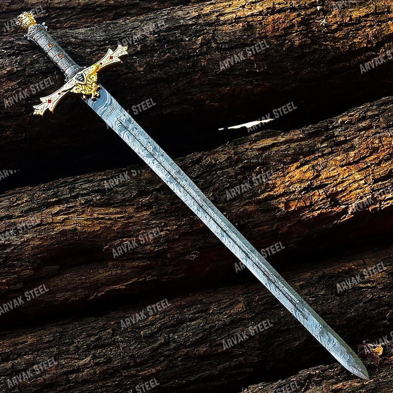May include: A long, ornate sword with a patterned blade and a gold-colored hilt. The hilt features intricate designs and red accents. The sword is displayed against a backdrop of textured, dark brown wood. The text "ARVAK STEEL" is visible on the blade.