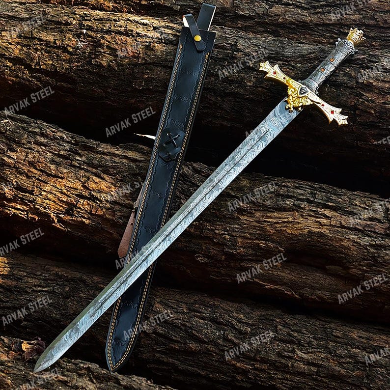 May include: A decorative sword with a patterned blade and ornate gold hilt, featuring red accents. The sword rests beside a black leather sheath. The blade has the text "ARVAK STEEL" printed on it.