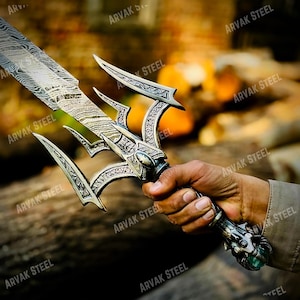 May include: A detailed view of a decorative sword with a silver-colored handle and blade. The blade has a unique pattern, and the handle features intricate designs. The sword is held in a hand, showcasing its craftsmanship.