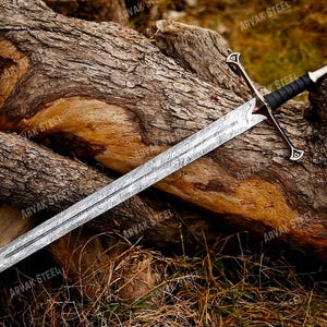 May include: A long, silver sword with a patterned blade rests on a weathered log. The sword features a black handle and a silver crossguard and pommel. The blade has a detailed, textured design. The sword is a fantasy or historical item.